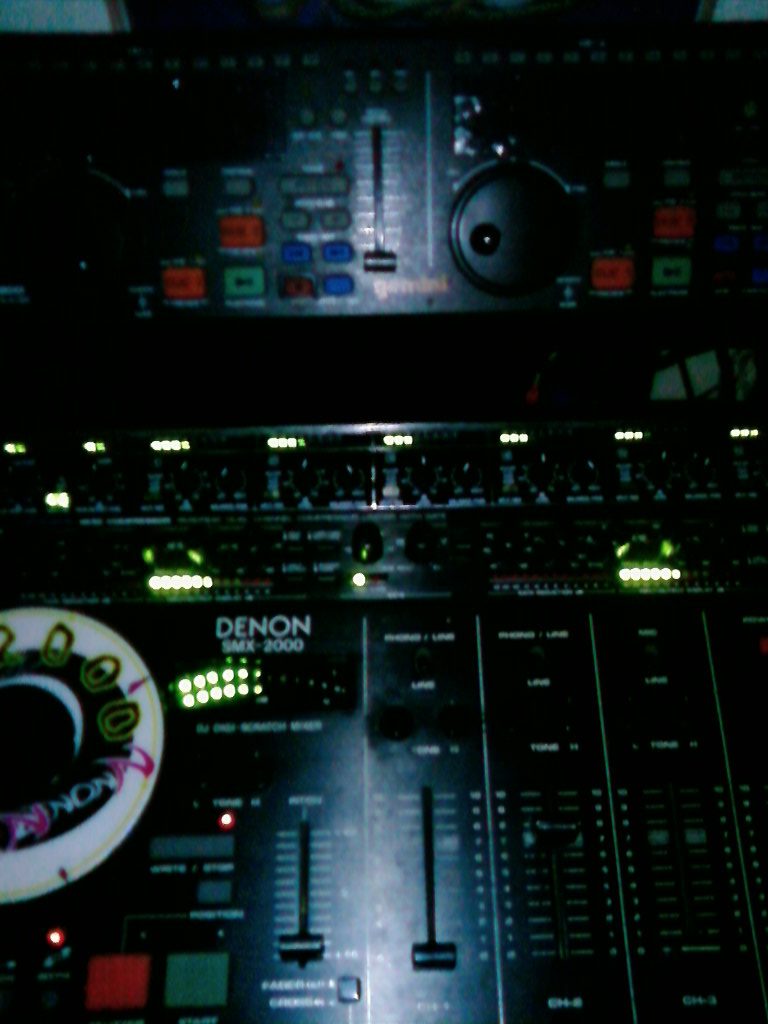 Close-up of a Denon SMX-2000 scratch mixer and Gemini CD-9800 dual CD player in a dark room